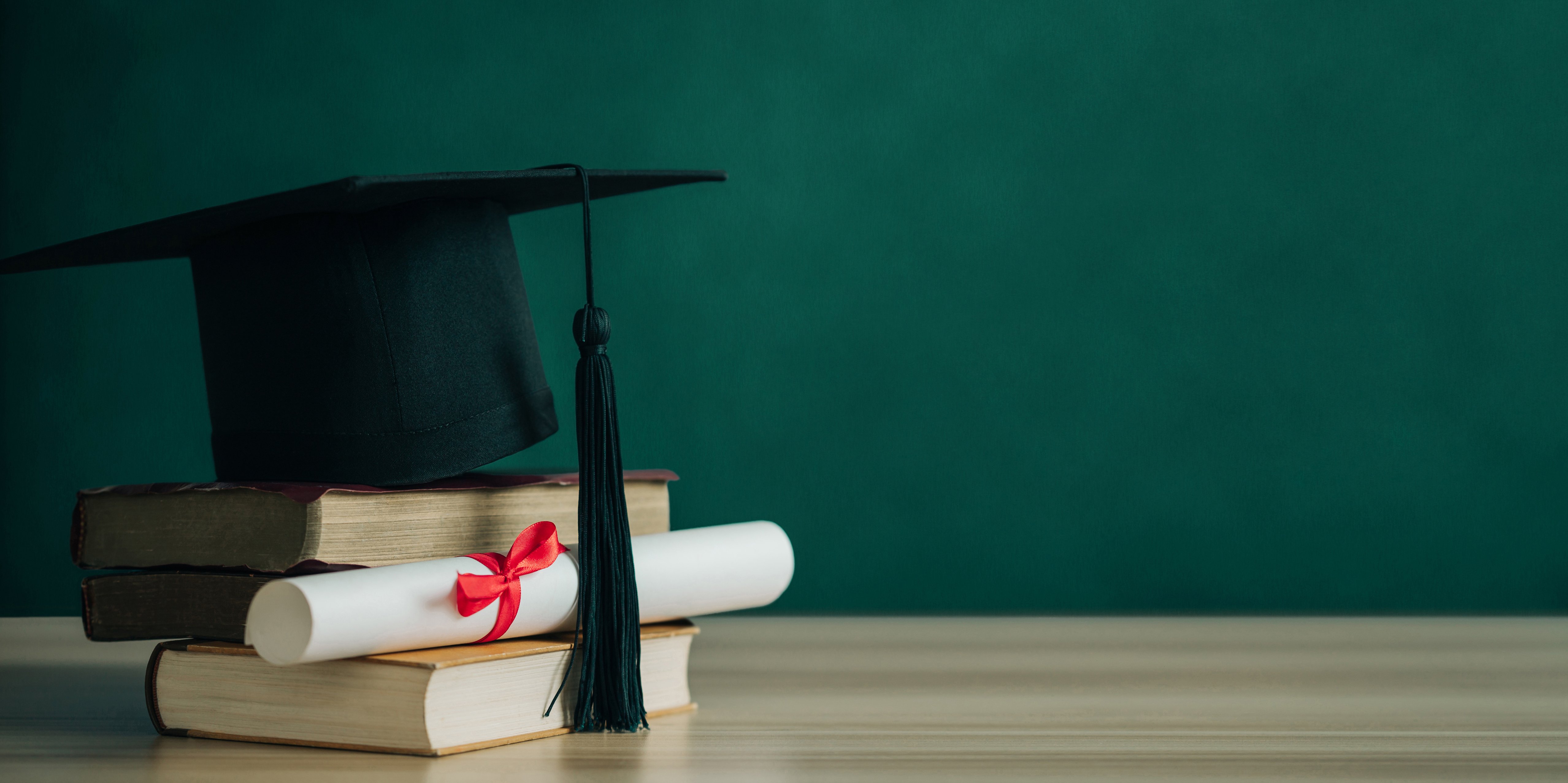 A mortarboard and graduation scroll, tied with red ribbon, on a